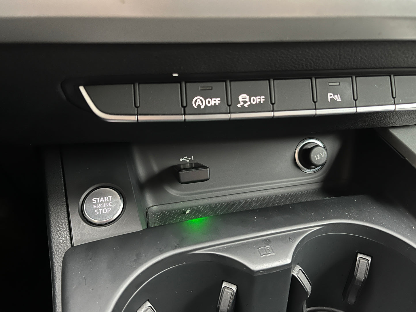 Close-up of a car dashboard featuring start/stop button and controls for wireless connectivity.